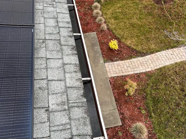 A clean gutter run beside roof solar panels, looking down over the garden