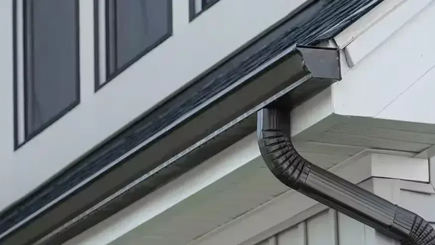 A dark-finish gutter run with its downspout elbow turning down the wall