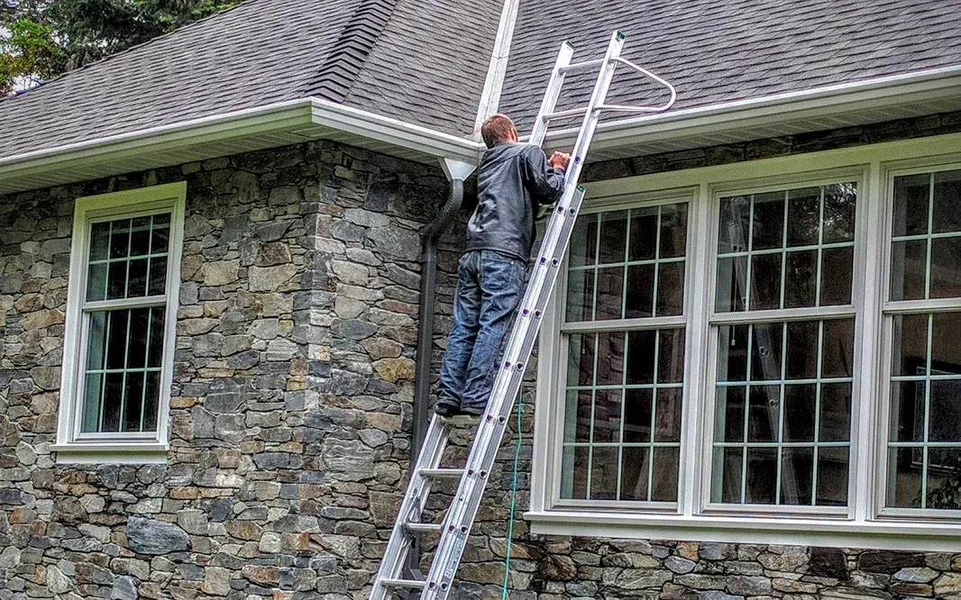 Extension ladder against a stone house, a worker up at the gutter line